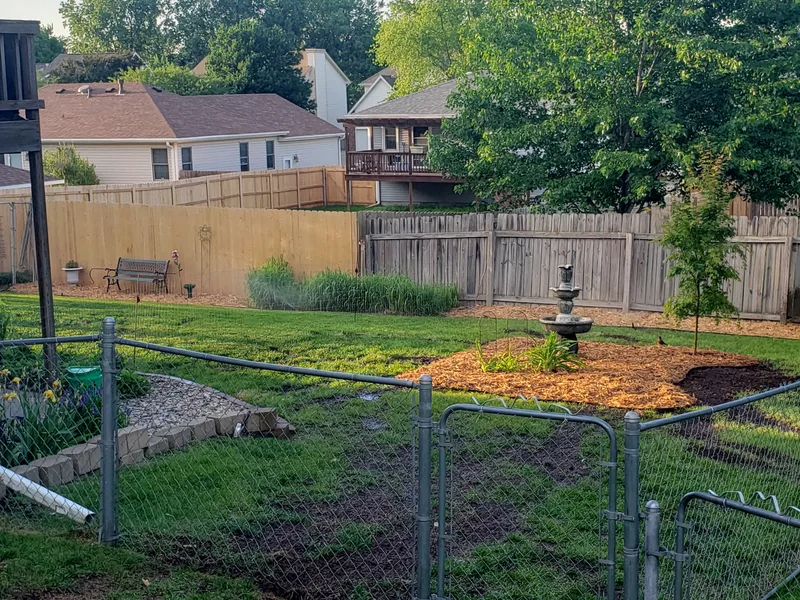 Landscaped residential backyard in Lincoln, Nebraska with green lawn, garden beds, birdbath, and wood privacy fence