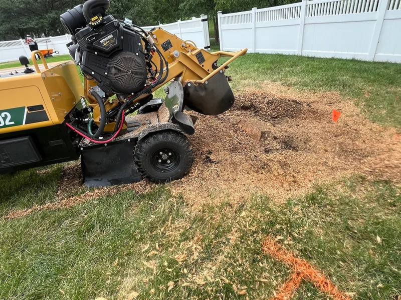 SC402 stump grinder actively grinding a stump beside a white vinyl fence in a Lincoln, Nebraska backyard